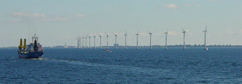 Multiple Danish wind turbines lined up on water.